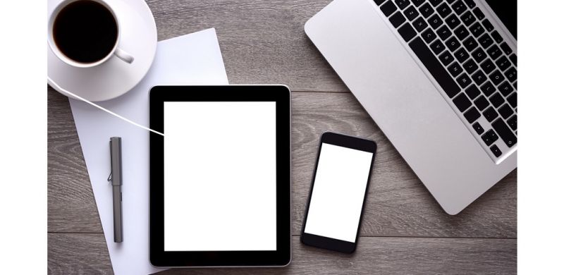 Digital tablet, laptop and smart phone on a business desk with blank white screens.